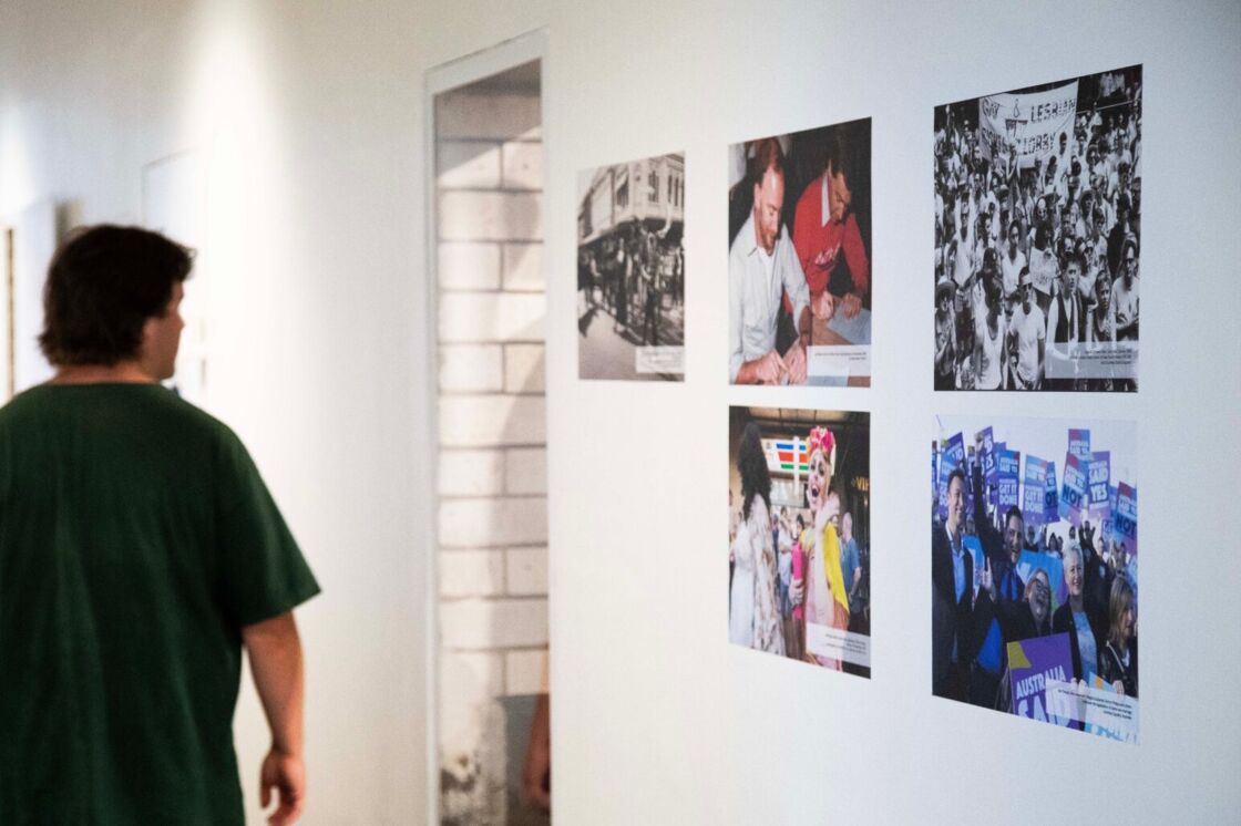 A young man walks past an archive photo wall of Australians protesting for gay rights at Qtopia Sydney.