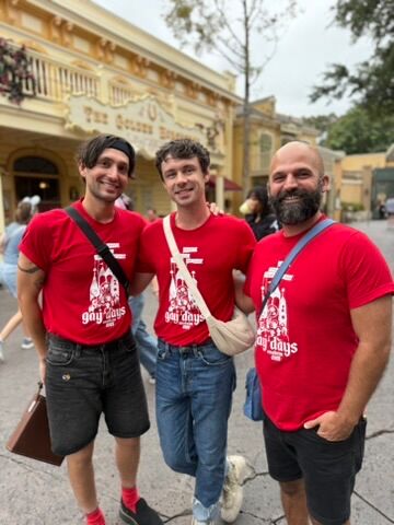 Three men pose and smile in red shirts on Main Street at Disneyland during Anaheim Gay Days.