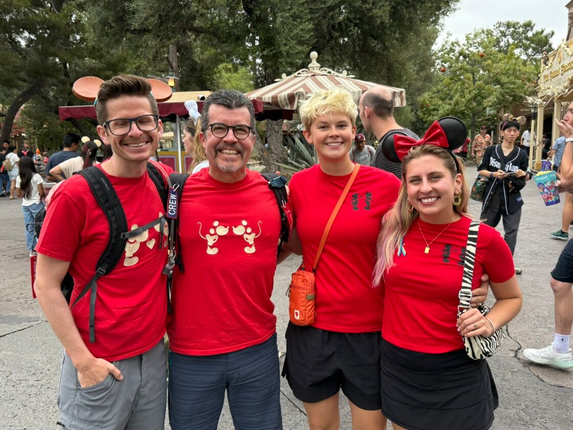 A group of two men and two women smile with their arms around each other in red t-shirts at Disneyland's Anaheim Gay Days.