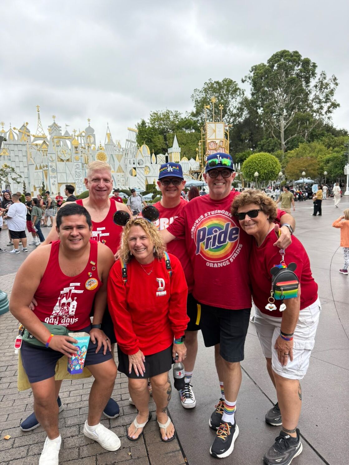 A group of six men and women smile in red shirts outside of It's a Small World at Anaheim Gay Days at Disneyland.