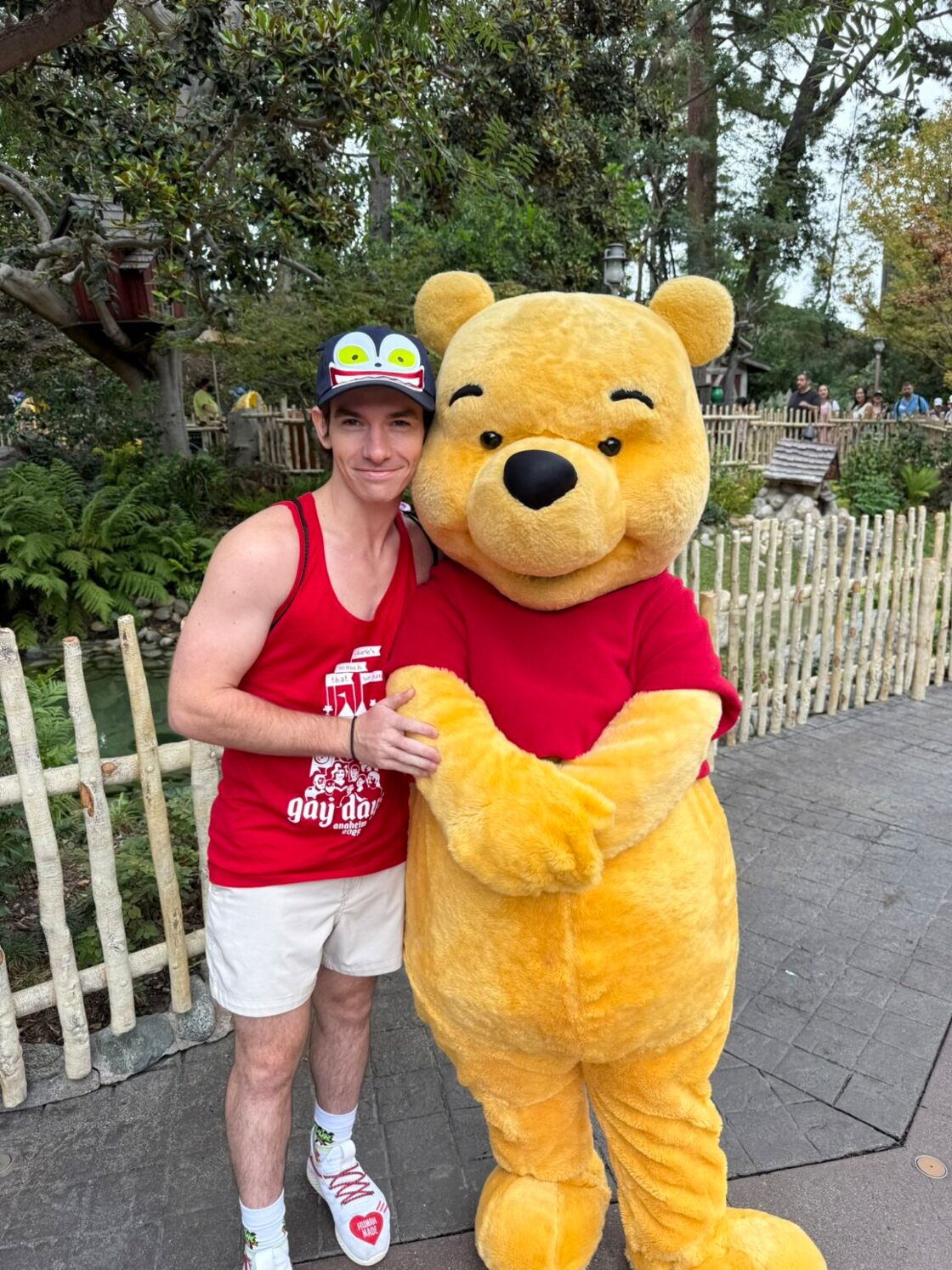 A young man in a red tank top poses with Pooh Bear at Disneyland's Anaheim Gay Days.