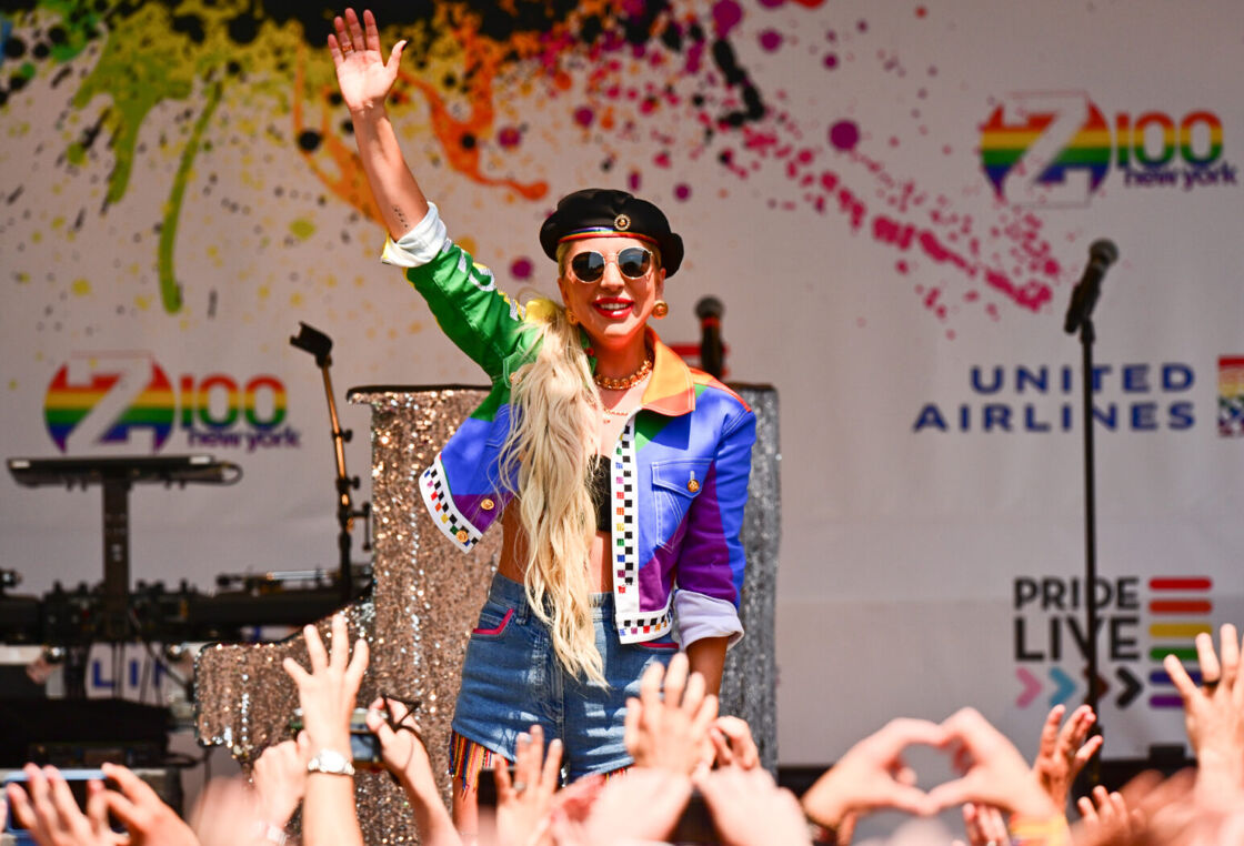Lady Gaga waves on stage in a rainbow colored ensemble outside of the Stonewall Inn.