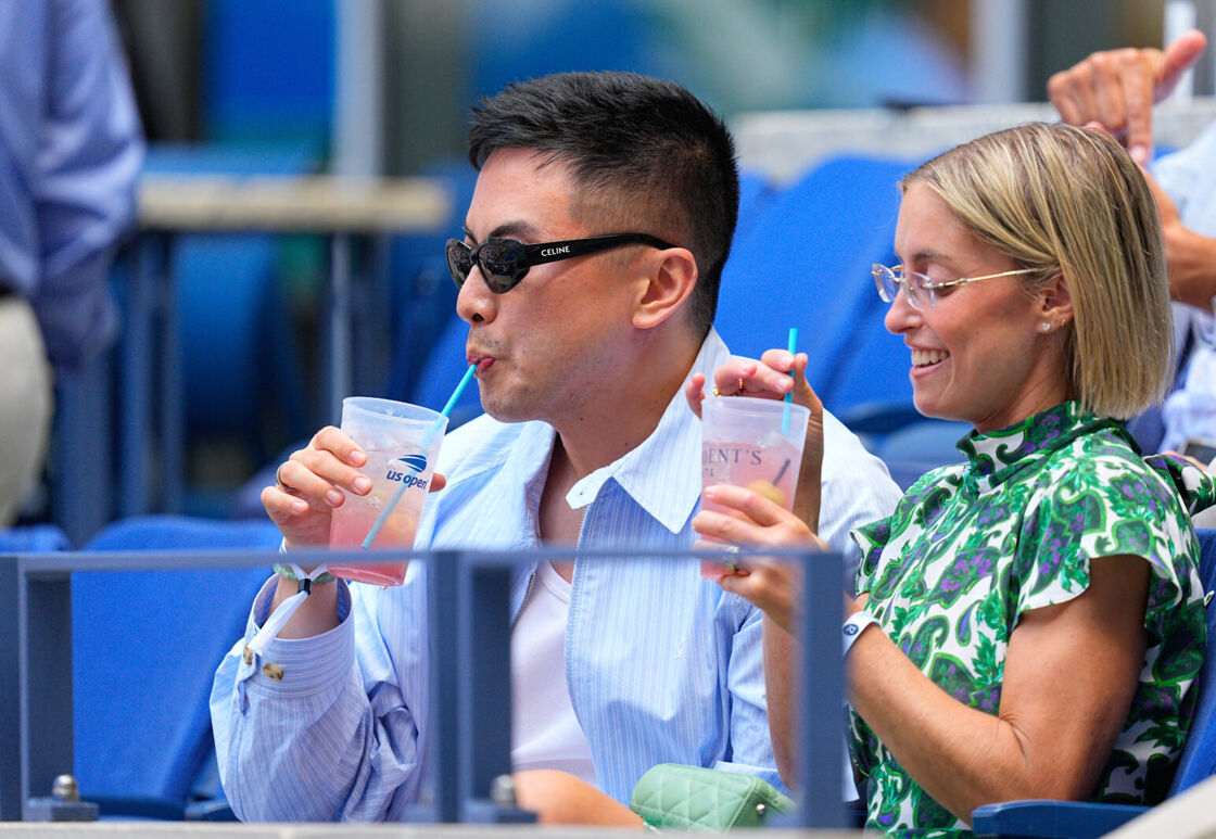 Bowen Yang sips a cocktail while wearing sunglasses at the US Open.