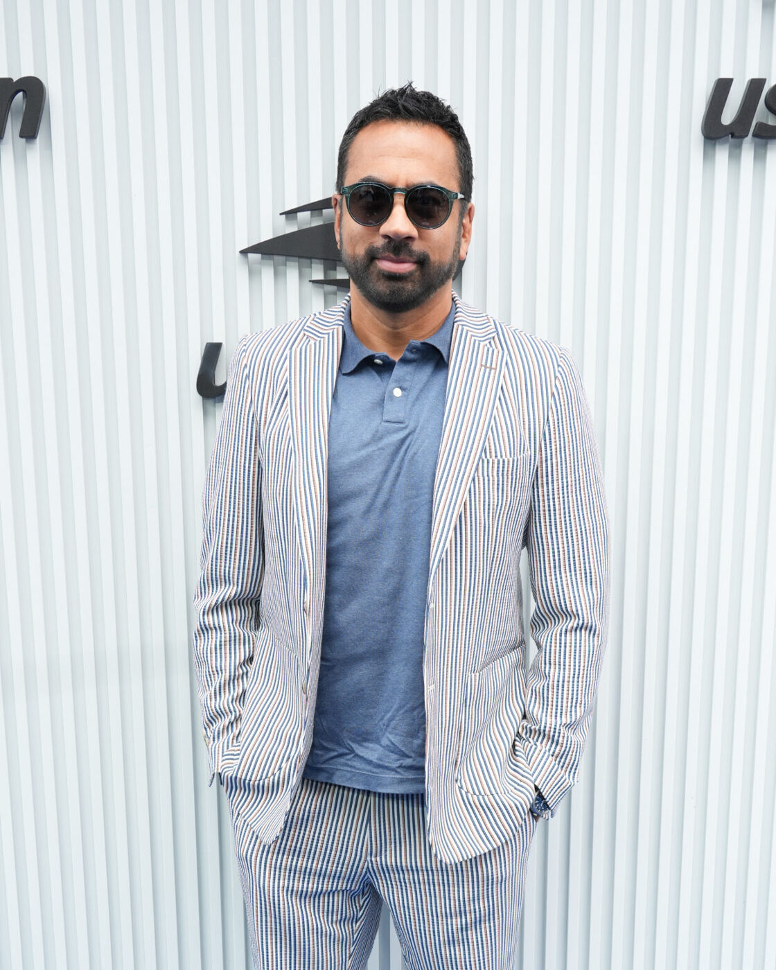 Kal Penn smiles softly while wearing sunglasses at the US Open.