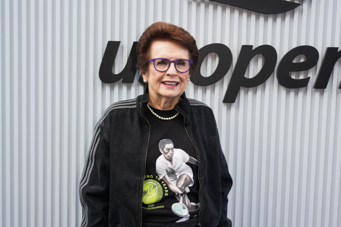 Billie Jean King smiles in a black jacket and tennis t-shirt at the US Open.
