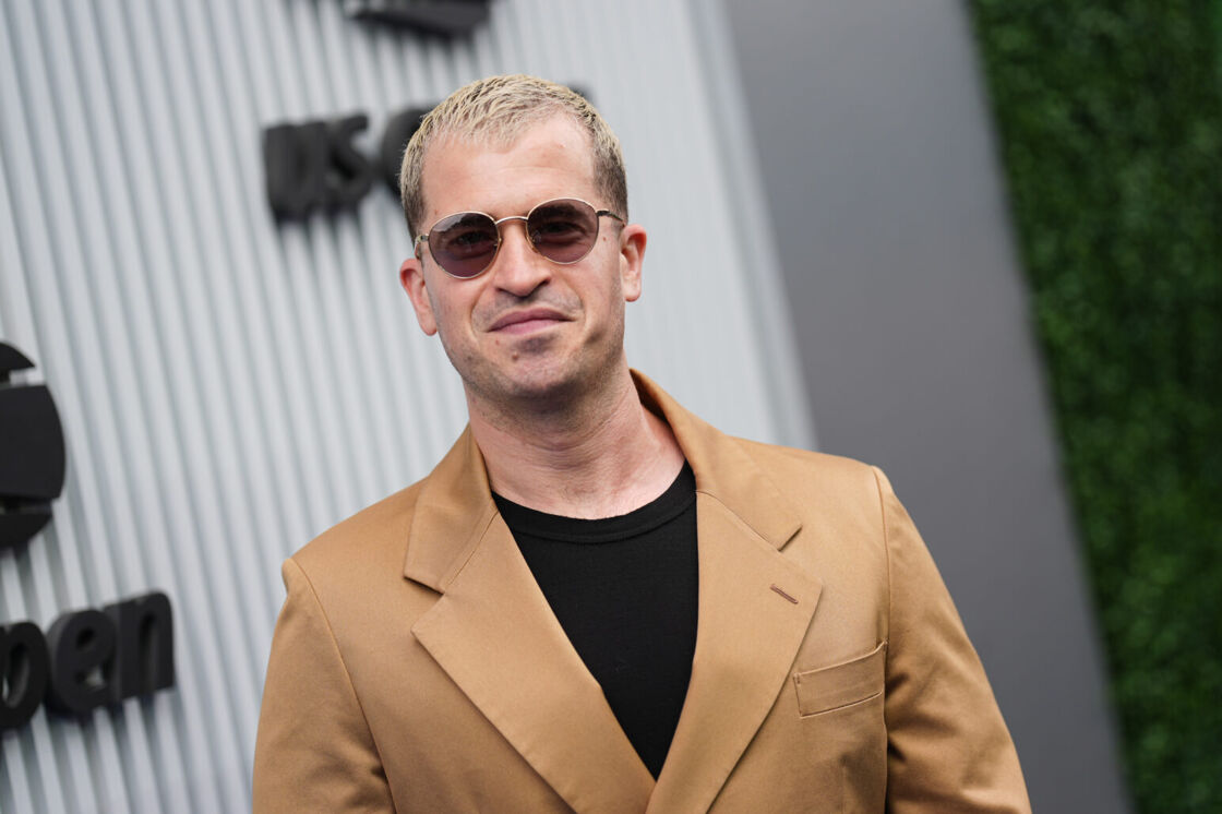 Evan Ross Katz smiles in a brown suit jacket and sunglasses at the US Open.