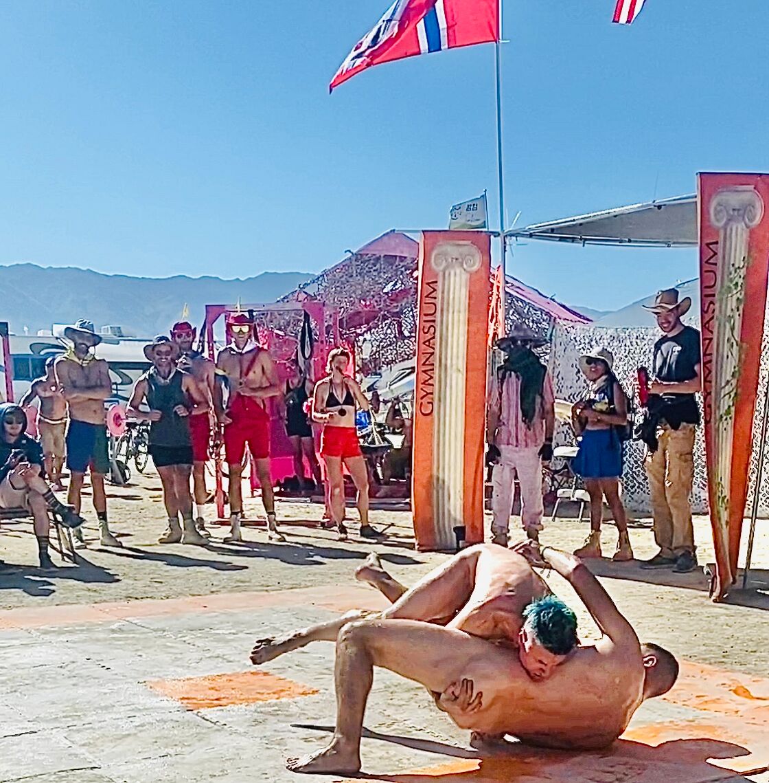 Queer Burners competing in a Naked Oil Wrestling competition at Burning Man 2024.