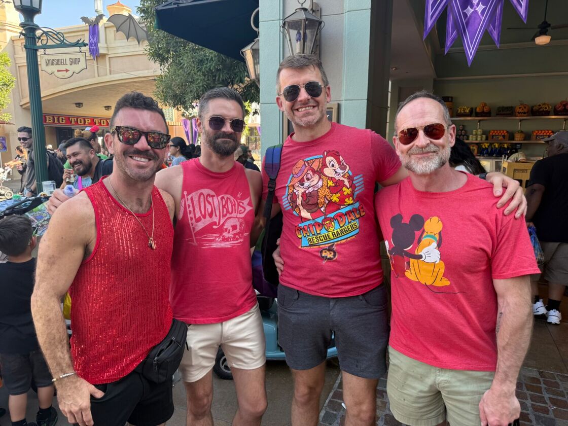 A group of four men in sunglasses smile in red shirts at Anaheim Gay Days.