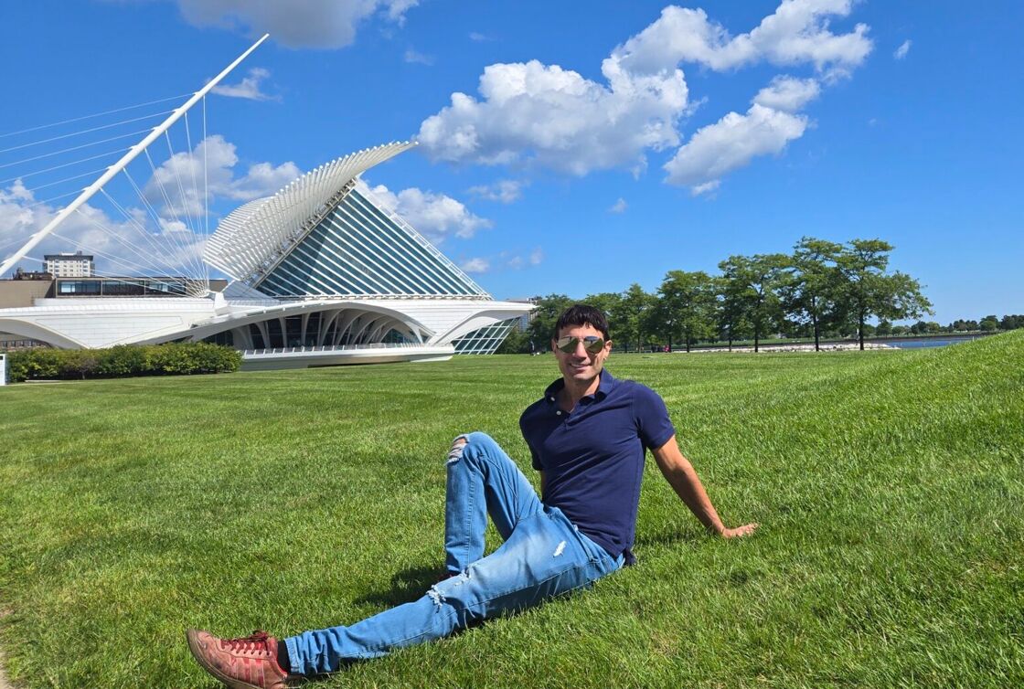 Author Joey Amato poses in the grass in front of the Milwaukee Art Museum.