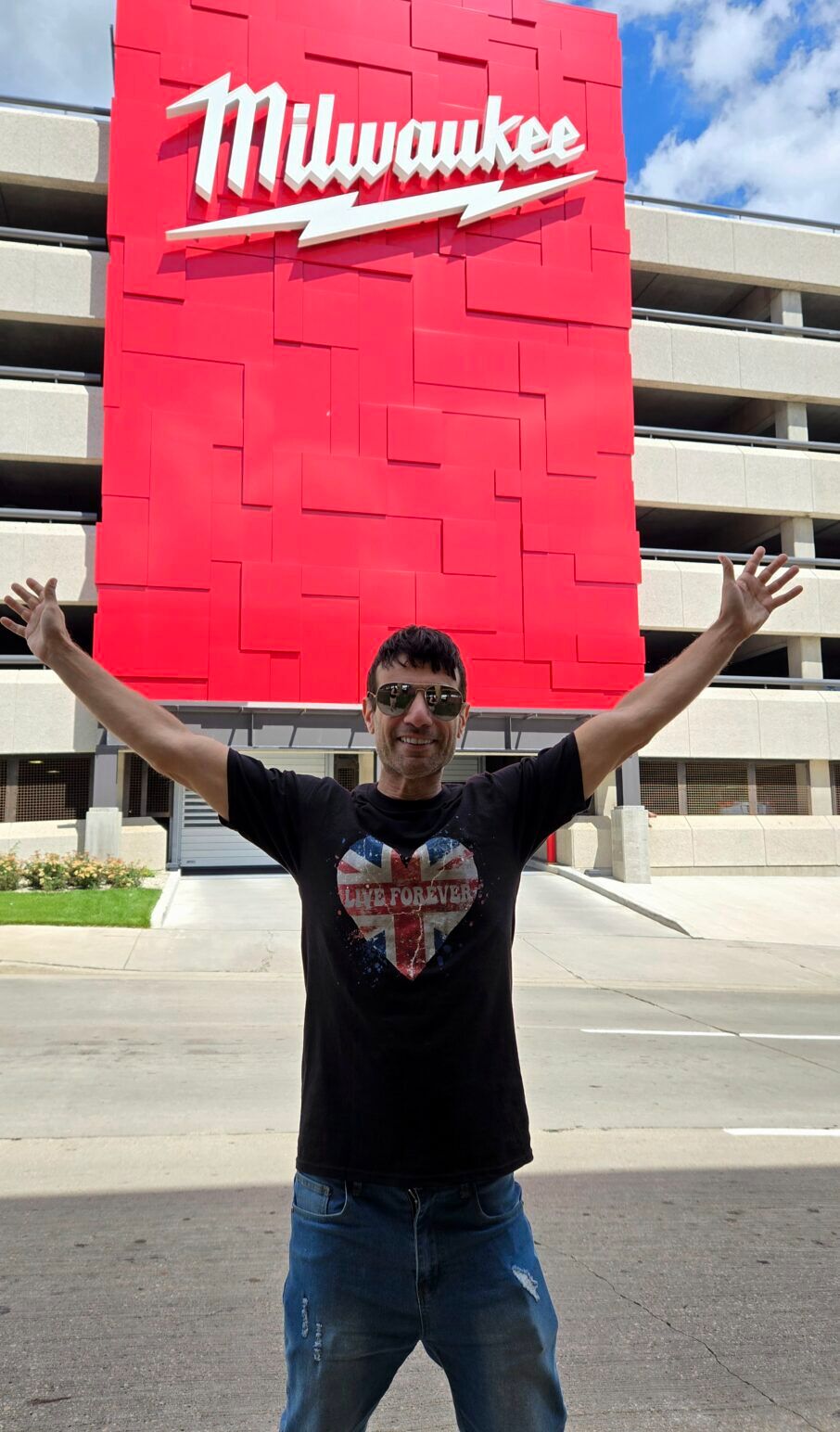 Author Joey Amato poses in front of a big red sign that says "Milwaukee" with his arms spread open.