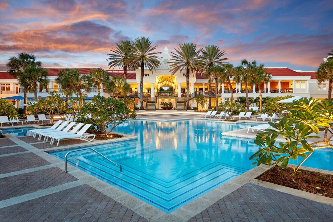 A pool surrounded by palm trees and loungers, pictured at sunset at Curaçao Marriott Beach Resort.
