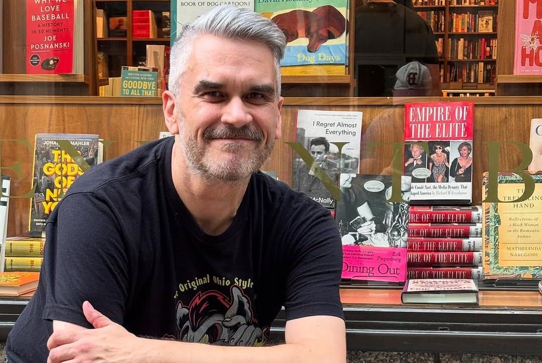 Journalist Erik Piepenburg stands next to his book "Dining Out" in a bookstore window.