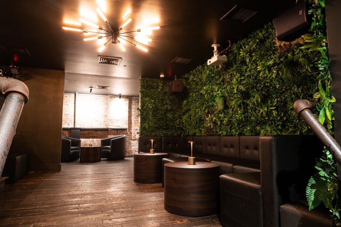 A seating area at G Lounge with thin brown couches and a green decorative wall behind it.