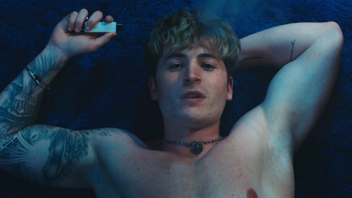 A blonde shirtless man poses mysteriously hitting a vape in a scene from "Blue Film."