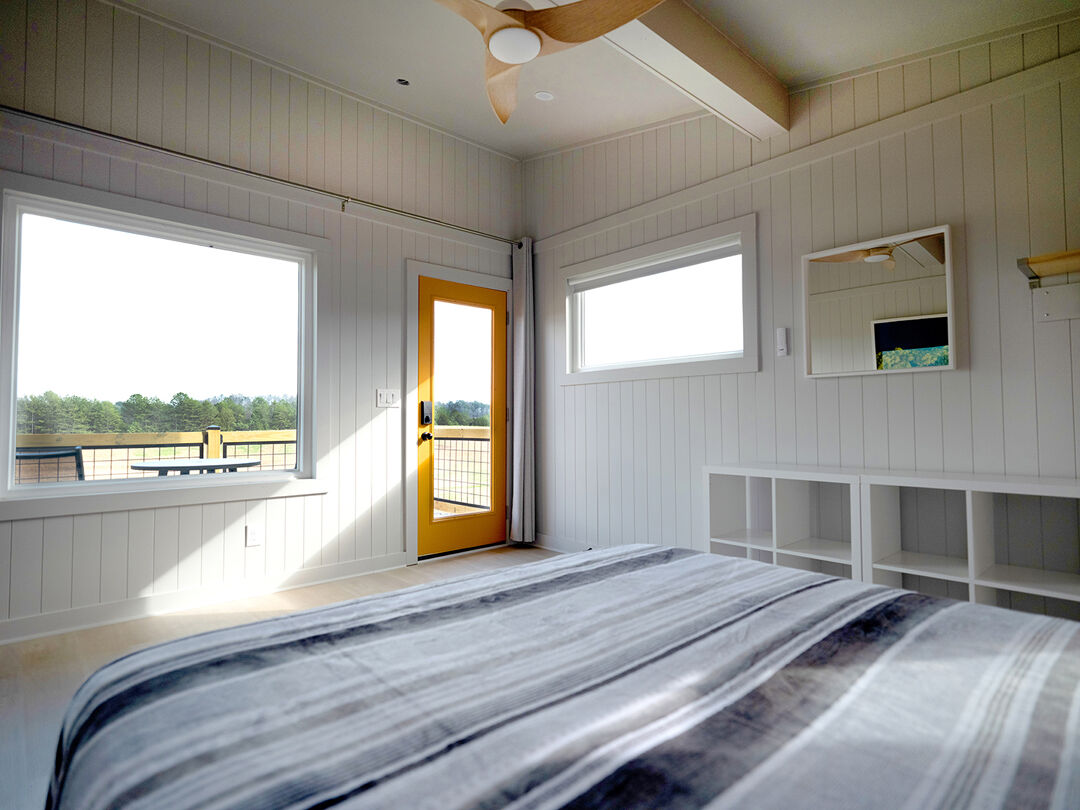 The interior of a cabin at Blue Moon Campground, showing off a scenic patio view, clean white walls, shelving, and a spacious bed.