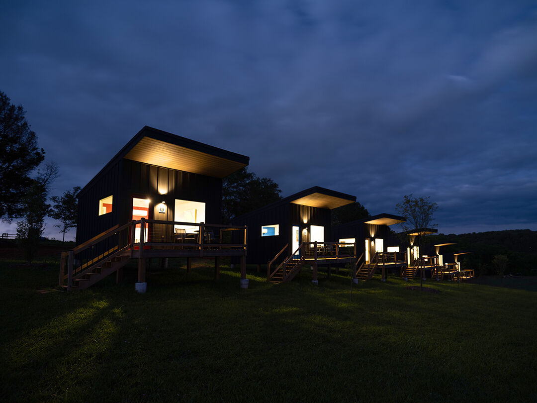 A line of custom-built cabins at Blue Moon Campground are lit up against the dark night in the woods.