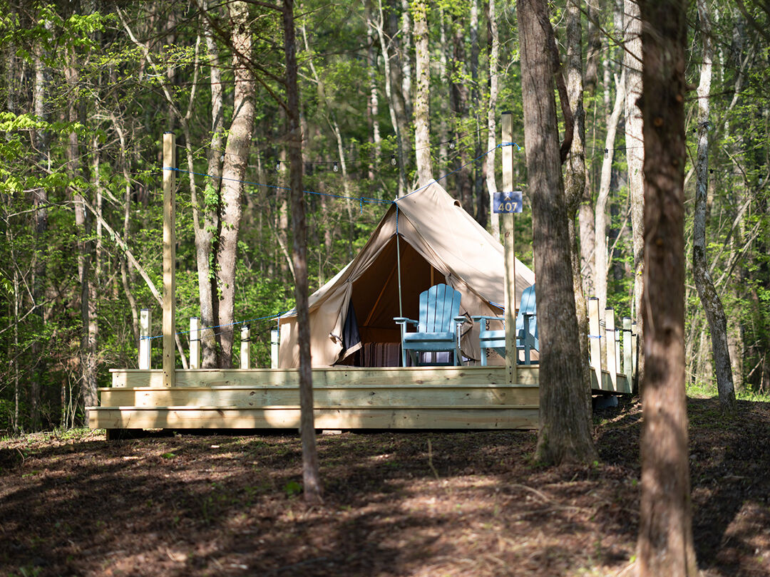 A glamping tent is pictured among trees with a small wooden patio in front of it at Blue Moon Campground.