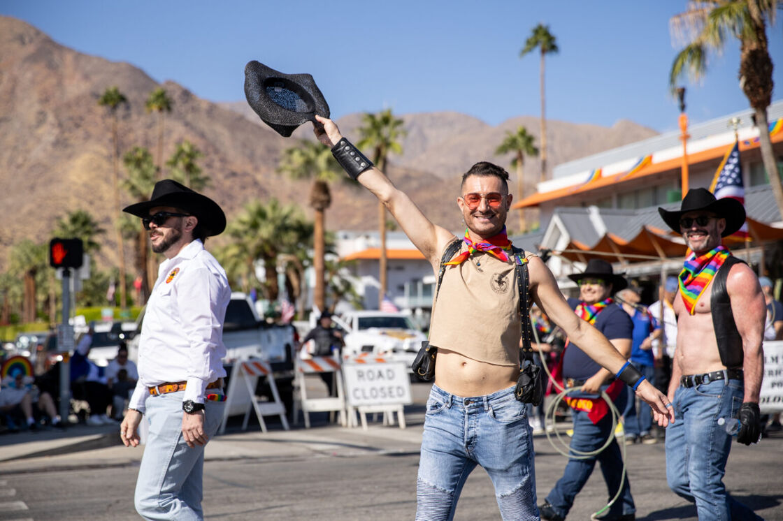 A Palm Springs Pride attendee holds up a cowboy hat while walking down the streets of Palm Springs.