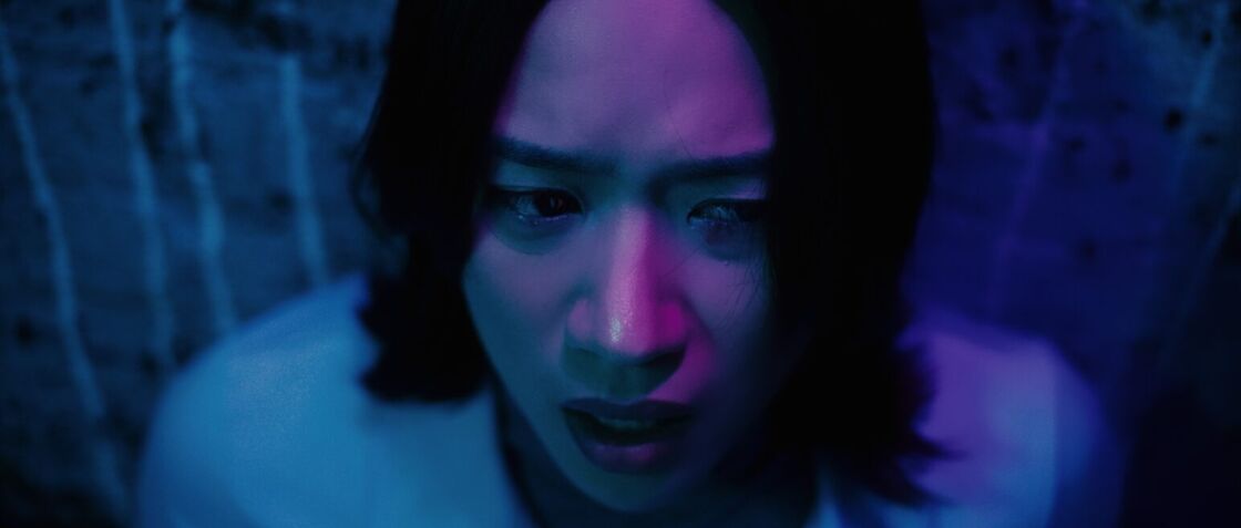 An actress stares off in blue hued lighting looking unsettled in a scene from "Dolls."
