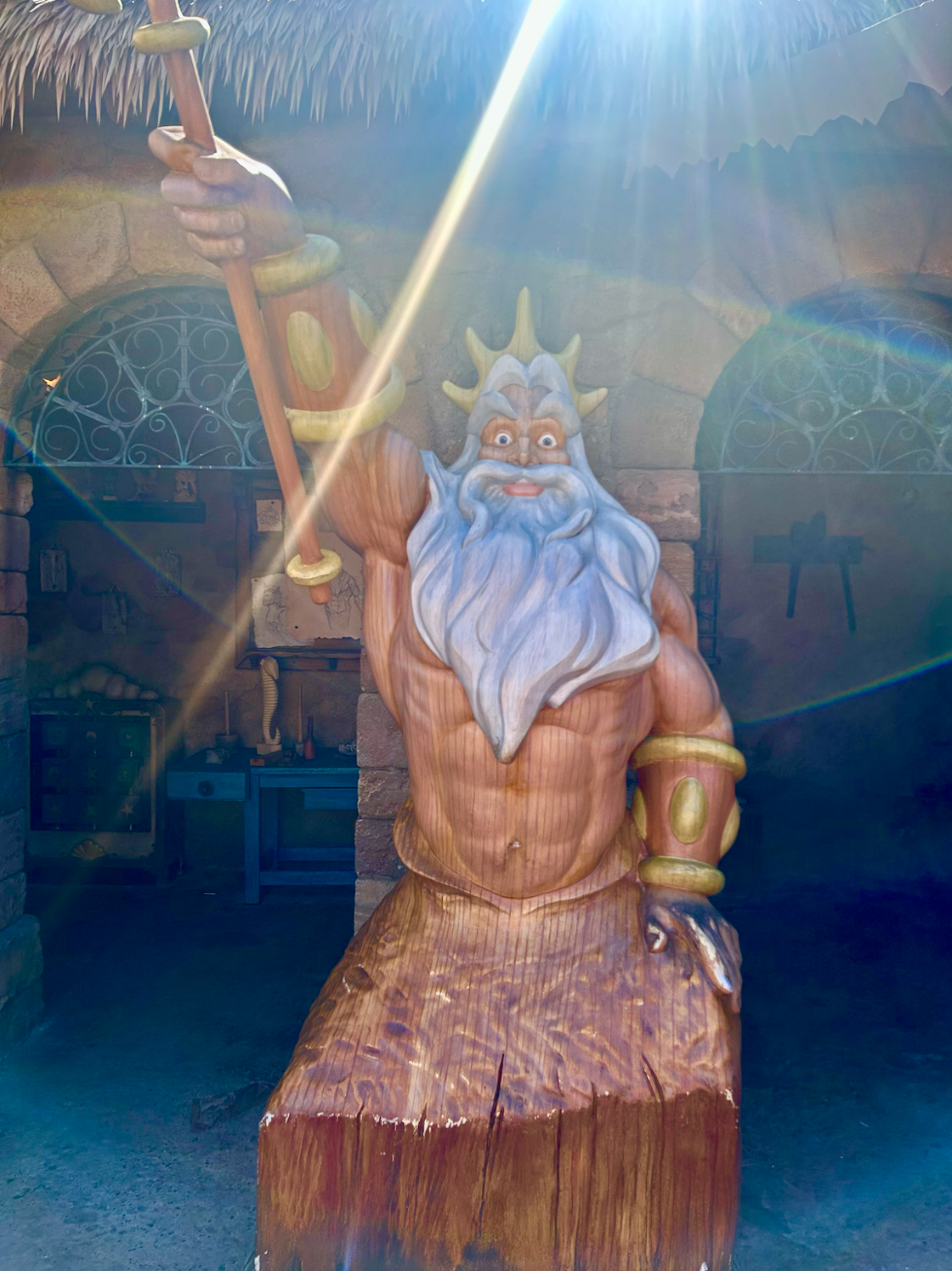 A wooden statue of King Triton from "The Little Mermaid" on display at Disney World shown on a sunny day.