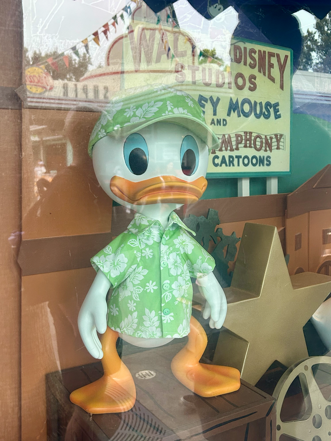 A statue of an animated duck stands wearing a floral printed hat and a buttoned down t-shirt. 