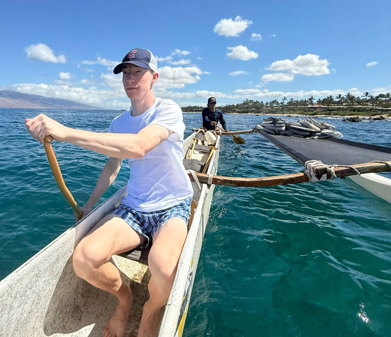 A young man sits on an outrigger at the Andaz Maui in the middle of a scenic ocean.