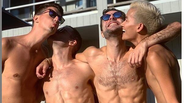 Four shirtless guys embracing in the sun.