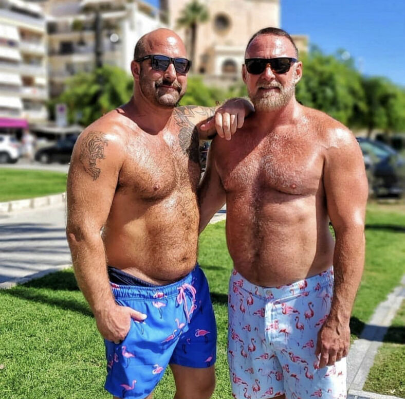 Two men shirtless in swim trunks on grass