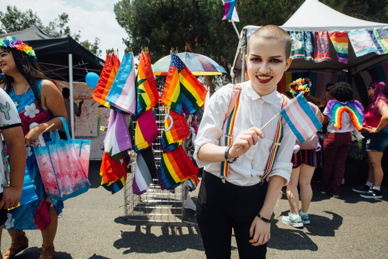 A person in suspenders holds a small trans flag