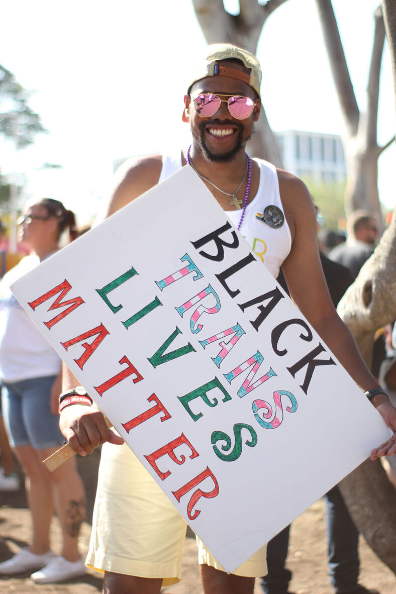 A smiling man holds a sign reading 'black, trans lives matter'