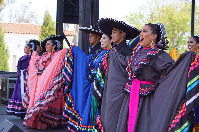 A group of performers in colorful Latin-American garb stand together on stage