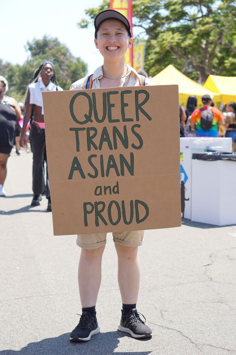 A smiling person holding a sign that reads 'Queer, trans, Asian and proud'