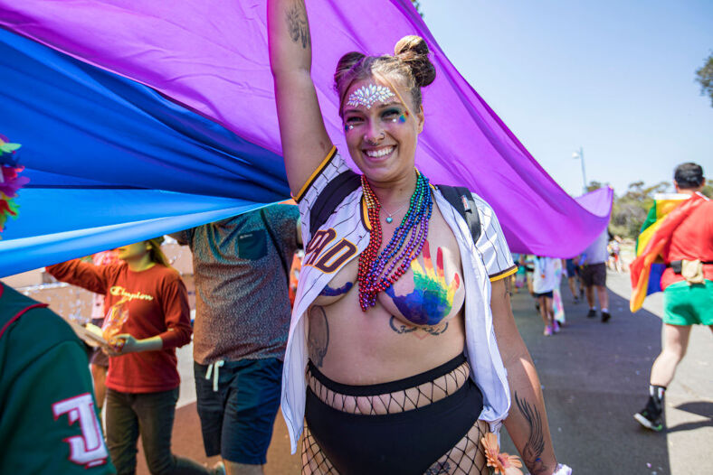 A woman with rainbow handprints on her chest smiles proudly at the camera