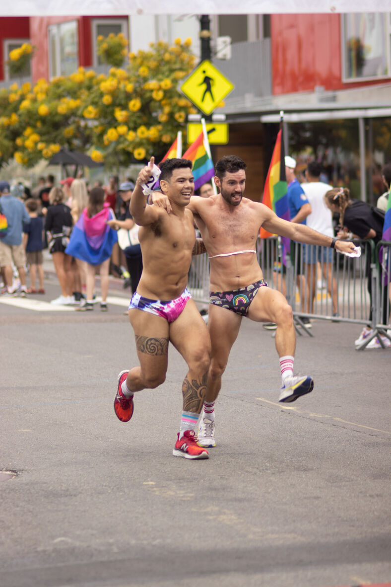 Two men in colorful underwear skip down the street