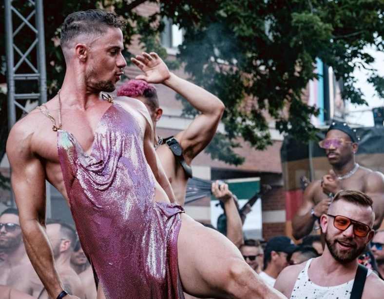 Muscular man in a pink sequin dress dances above a crowd