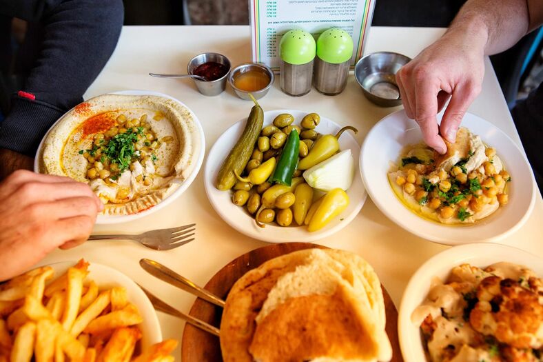 Plates of hummus, pita bread, french fries, pickled olives and vegetables cover a dinner table.